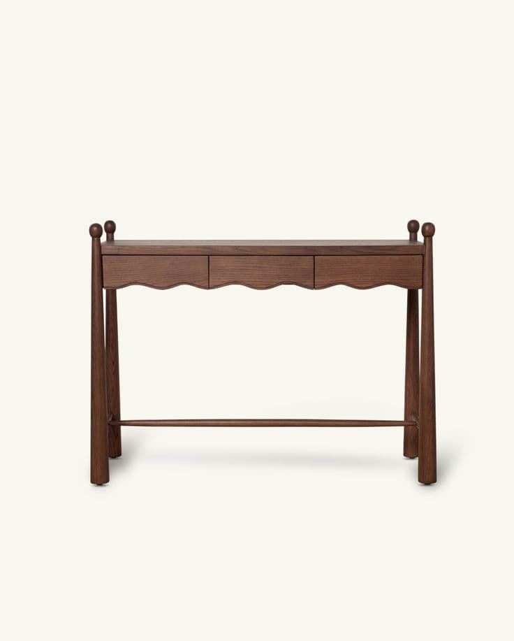 A long and narrow dark brown wooden console table featuring a rectangular top. It includes two drawers with distinctive scalloped front panels. The table is supported by four turned, tapering legs that extend above the tabletop, each topped with a spherical finial. A horizontal stretcher bar connects the legs near the base, providing stability. — 3D model