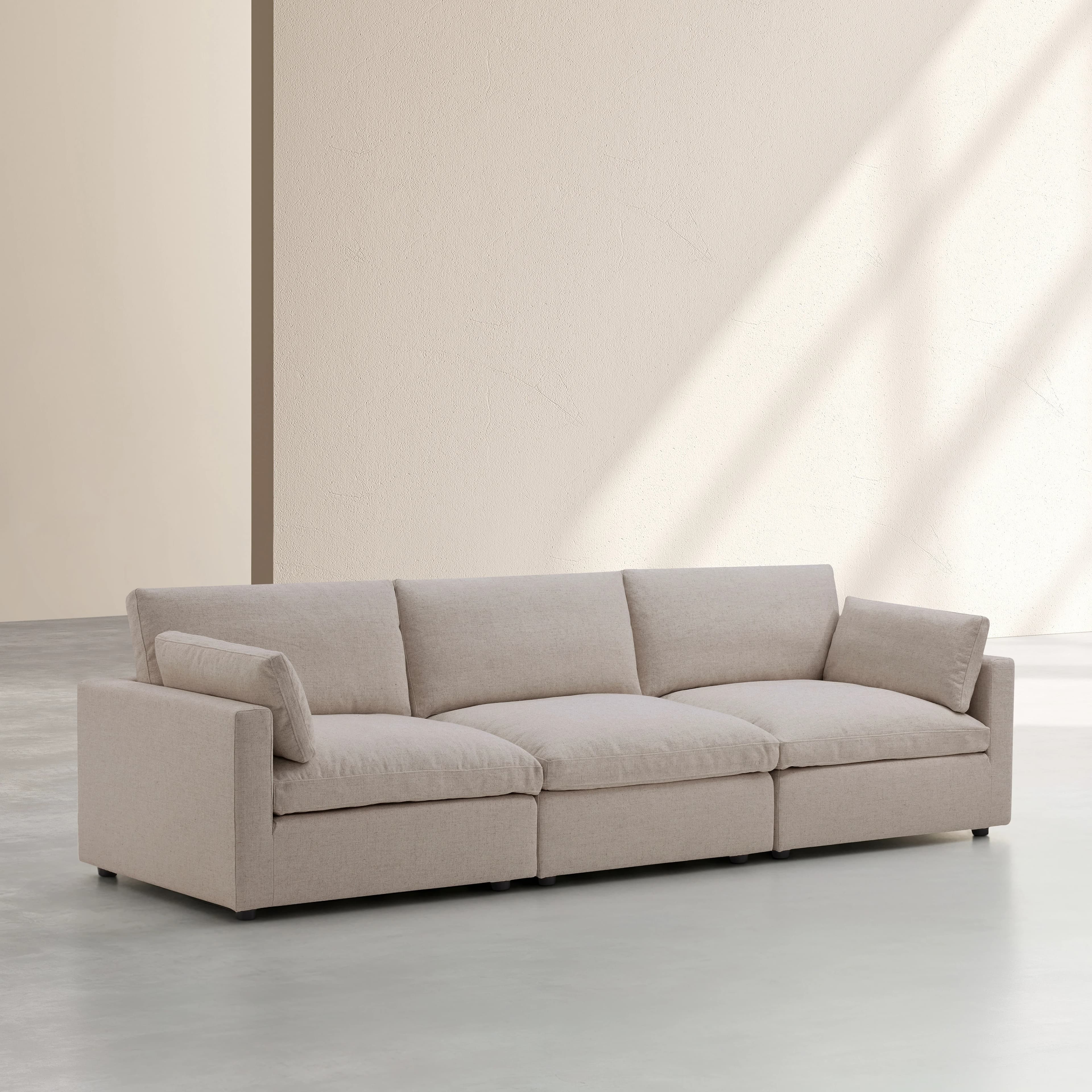 A three-seater sofa with a low profile and wide arms. The sofa features deep seat cushions and back cushions, with an additional bolster pillow on each side. The upholstery appears to be a textured fabric. It is supported by short, dark-colored legs. — 3D model