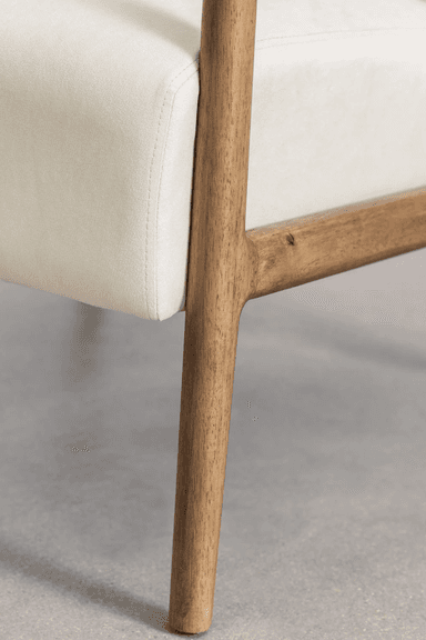 A close-up view of the base of an armchair, showing the junction of a cream-colored upholstered seat and a wooden frame. The wooden elements appear to be made of a light to medium-toned wood with visible grain, exhibiting a smooth, finished surface. The upholstery is subtly textured and features clean stitching lines. The overall design suggests a modern or mid-century modern aesthetic. — 3D model