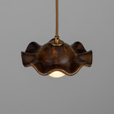 A pendant light featuring a distinctive wavy, shell-like metal shade with a mottled, patinated bronze finish. Suspended beneath the shade is a spherical frosted glass diffuser, emitting a soft, warm light. The fixture hangs from a braided textile cord, connecting to the shade via a small brass fitting. — 3D model
