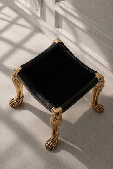 A low, square-shaped ottoman featuring a black velvet upholstered top set within a black lacquered frame. It stands on four highly ornate, gilded metallic legs, sculpted with lion's heads at the top and lion's paws as feet. — 3D model