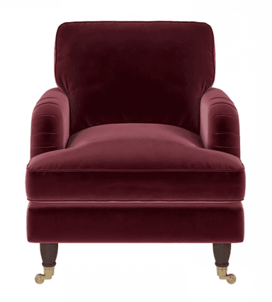 A deep red, velvet upholstered armchair featuring rolled arms with subtle pleating, a plush seat cushion, and dark turned wooden legs with brass casters. — 3D model