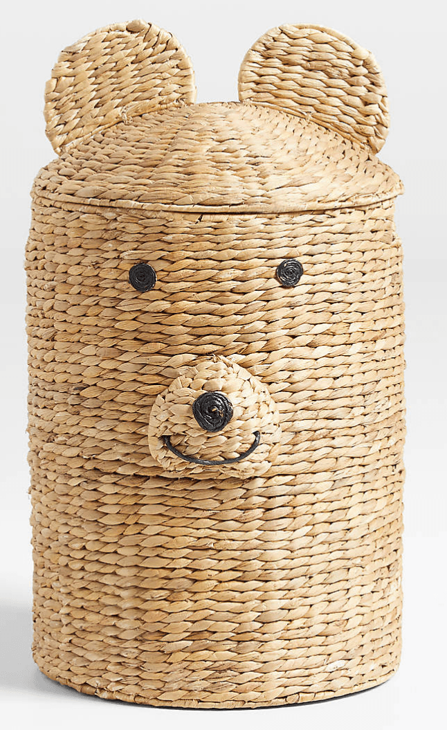 A natural fiber woven storage basket shaped like a bear, complete with rounded ears on the lid and stitched facial features. The basket has a cylindrical body and is constructed from tightly woven natural fibers, likely seagrass or water hyacinth, in a light, natural hue. The bear's eyes are represented by two small black button-like elements, and its nose and smile are formed from black stitching. The lid fits snugly over the basket's opening. — 3D model