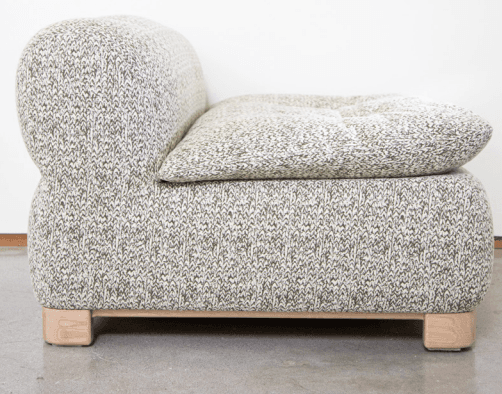 A contemporary armchair with a distinctive rounded silhouette. The piece is upholstered in a textured knit fabric with a marled pattern of light grey and white. It features a low profile, a generously padded seat cushion, and a softly curved backrest. The armchair is supported by a minimalist wooden base with four block-like feet. — 3D model