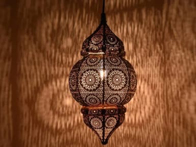 A highly decorative Moroccan-style pendant lantern, crafted from bronze-toned metal with intricate filigree patterns. The lantern features a distinctive two-part silhouette, with a dome-shaped top section merging into a larger, bulbous main body, both tapering to a pointed finial at the bottom. The entire surface is adorned with precise, laser-cut or hand-pierced geometric and floral motifs, designed to cast diffused and patterned light. — 3D model