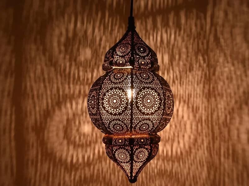 A highly decorative Moroccan-style pendant lantern, crafted from bronze-toned metal with intricate filigree patterns. The lantern features a distinctive two-part silhouette, with a dome-shaped top section merging into a larger, bulbous main body, both tapering to a pointed finial at the bottom. The entire surface is adorned with precise, laser-cut or hand-pierced geometric and floral motifs, designed to cast diffused and patterned light. — 3D model