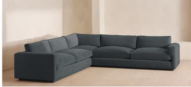 An L-shaped sectional sofa upholstered in a dark blue or slate-colored fabric. The sofa features a low profile, wide block arms, and loose back cushions, indicative of a contemporary minimalist design. It is composed of multiple modular sections that create a right-hand facing L-configuration, providing ample seating. — 3D model