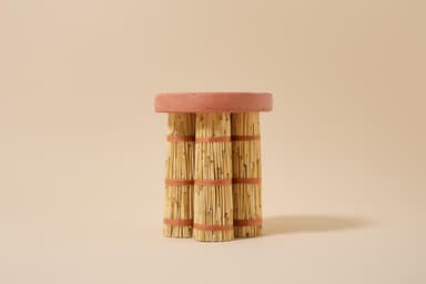 A small, round accent table featuring a flat, circular top made of reddish-brown terracotta. The base consists of three bundles of light-colored bamboo sticks, tied securely in multiple places with reddish-brown woven natural fiber. The legs appear to be cylindrical and provide a sturdy base for the rustic top. — 3D model
