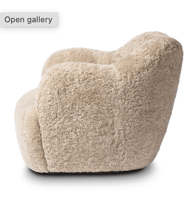 A plush armchair upholstered in a textured, curly, light beige material resembling sheepskin. The chair features a rounded silhouette with integrated armrests that flow into the backrest, and a deep, comfortable seat. The base is solid and integrated with the main body of the chair, lacking distinct legs. The overall design is compact and inviting. — 3D model
