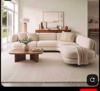 A cream or off-white L-shaped sectional sofa with soft, rounded edges, upholstered in a textured fabric. It features a main two-seat section connected to a single-seat section that extends into a chaise lounge, creating a corner configuration. The design is contemporary and minimalist, with clean lines and no visible legs or intricate detailing, suggesting a low-profile base. — 3D model