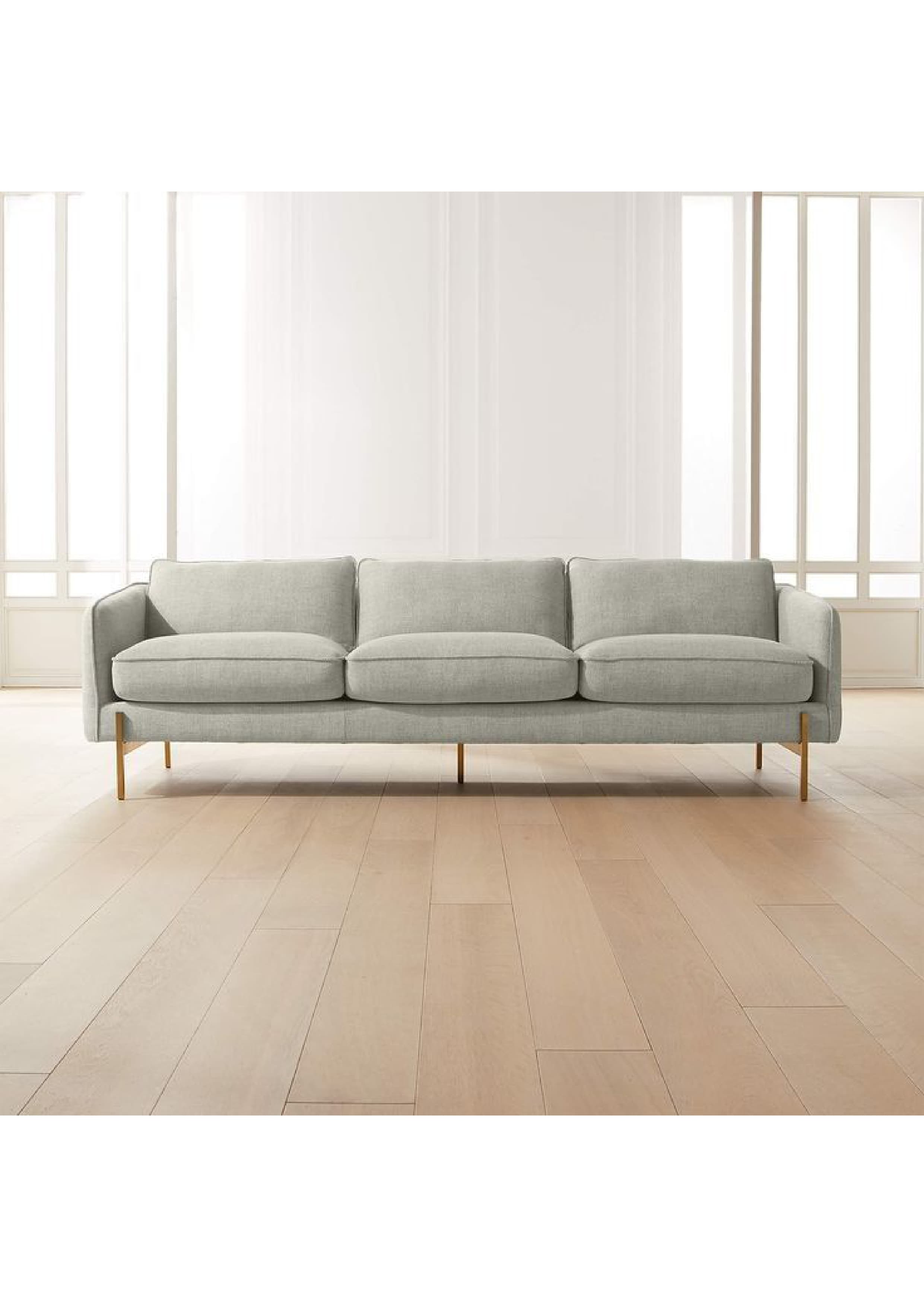 A modern three-seater sofa upholstered in a light grey fabric, featuring three distinct back cushions and three seat cushions. The sofa has slim, straight track arms that are upholstered in the same fabric as the body. It is supported by four slender, tapered metal legs with a brass or gold finish, providing a clean, elevated look. The overall design emphasizes minimalism and contemporary aesthetics. — 3D model