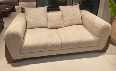 A contemporary two-seater sofa featuring a textured boucle-like fabric upholstery in a light, neutral color, combined with a dark wood base that curves upwards to form part of the armrests. The sofa includes two seat cushions and three loose back cushions. — 3D model