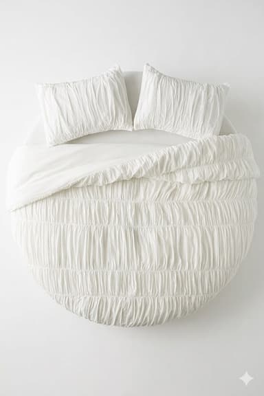 A top-down view of a circular platform bed adorned with a white shirred duvet cover and two matching shirred pillow shams. The bed base is a low-profile white circular platform, visible around the edges of the bedding. The bedding fabric exhibits a crinkled, textured appearance due to the shirring technique. — 3D model