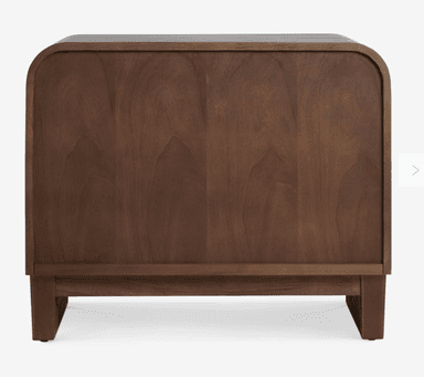 A contemporary nightstand featuring a dark-stained wooden frame with gently rounded top edges. It includes a single drawer with a woven cane front and a small brass knob, positioned above an open lower storage shelf. The base is a solid, plinth-like structure with subtle, short legs. — 3D model