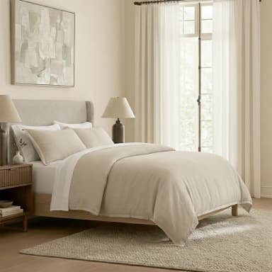 A bedroom scene featuring a bed, nightstand, artwork, and window treatments. The bed has a light-colored upholstered headboard and a duvet cover in a neutral tone. A wooden nightstand with ribbed drawer fronts is positioned to the left of the bed. An abstract painting hangs on the wall above the headboard. Sheer curtains cover a window behind the bed. — 3D model