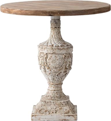 A rustic-style accent table featuring a round, light wood planked top and a highly ornate, distressed whitewashed pedestal base. The base has a detailed urn-like shape with decorative carvings and a square plinth foot, exhibiting a chipped paint finish with hints of a darker base showing through. — 3D model