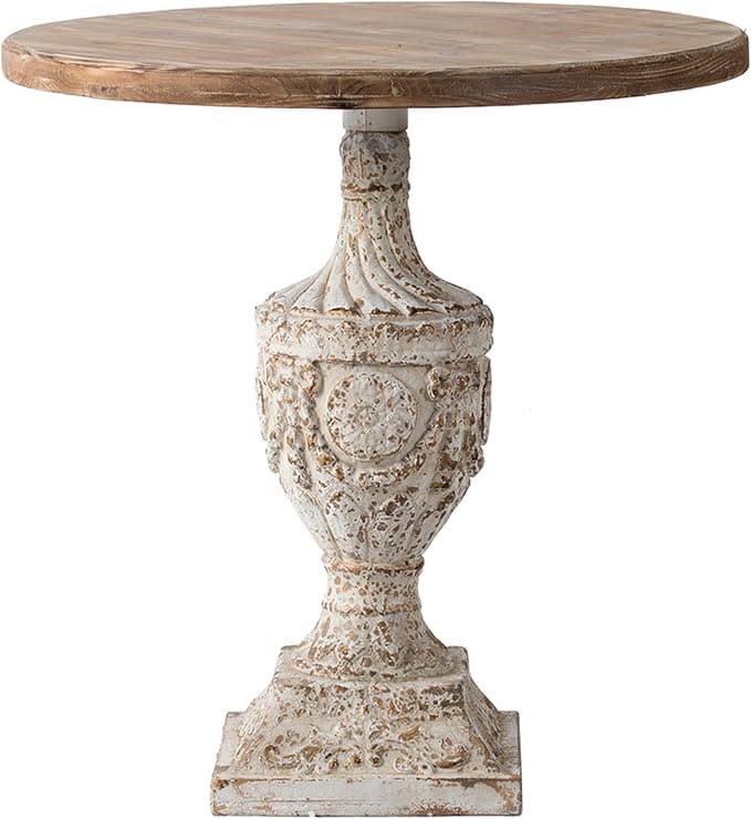A rustic-style accent table featuring a round, light wood planked top and a highly ornate, distressed whitewashed pedestal base. The base has a detailed urn-like shape with decorative carvings and a square plinth foot, exhibiting a chipped paint finish with hints of a darker base showing through. — 3D model