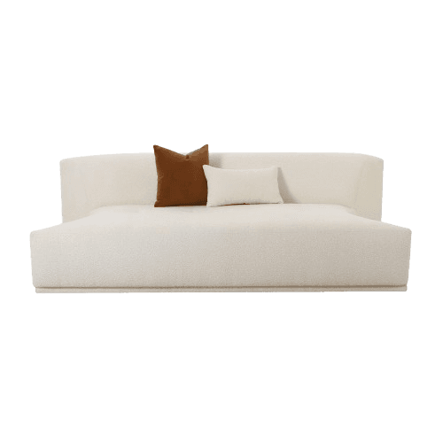 A contemporary daybed upholstered in cream bouclé fabric, featuring a low profile and a gently curved backrest that wraps around one side. Two accent pillows, one square in a rust brown velvet and one rectangular in cream bouclé, are placed on the seating surface. The design is minimalist and emphasizes comfort and lounging. — 3D model