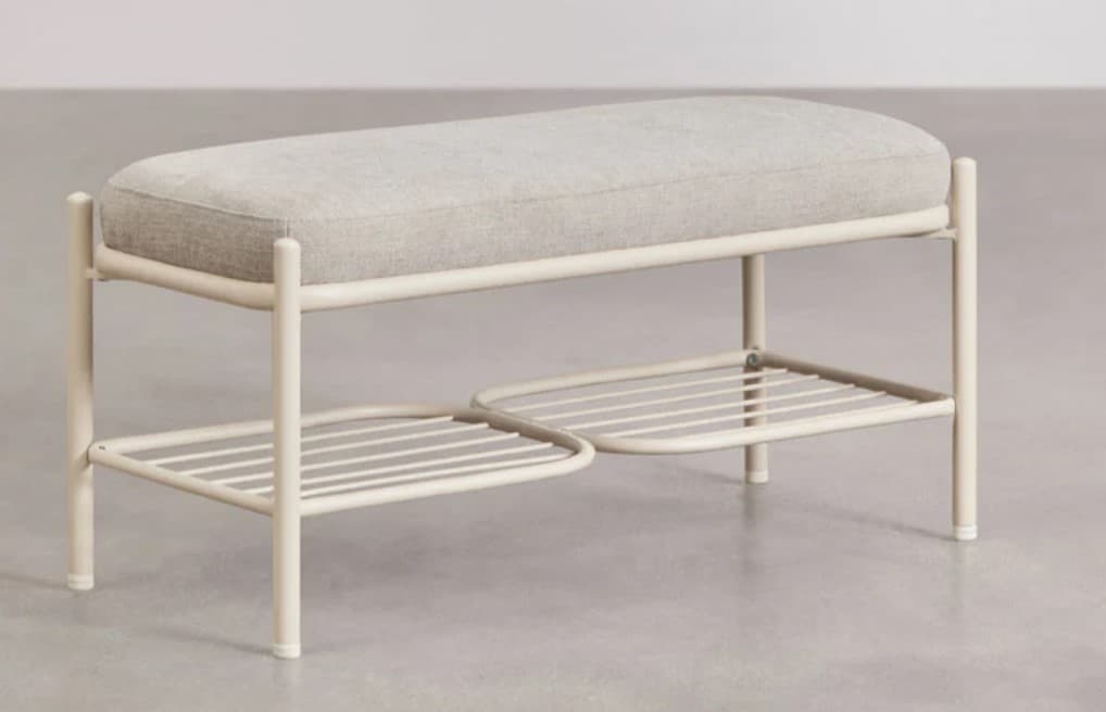 A minimalist bench with a padded seat and two tiered slatted shelves below. The frame is constructed from rounded metal tubing, painted in a light cream or off-white color. The top seat is upholstered in a textured, light grey fabric. The lower shelves have a slatted design for ventilation or drainage and are positioned at different heights, with a slightly curved outer edge on the front shelf. — 3D model