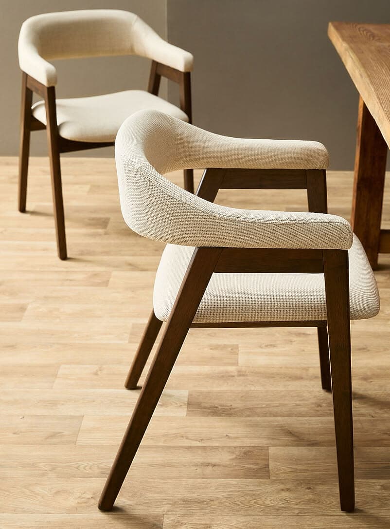 A modern armchair featuring a dark wood frame and cream-colored textured upholstery. The chair has a curved backrest that seamlessly transitions into integrated armrests. The four legs are slender and tapered, made from the same dark wood as the frame. The seat and back are fully upholstered, providing a comfortable and contemporary look. — 3D model