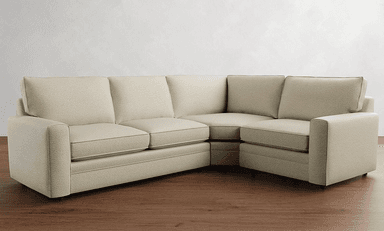 A sectional sofa with a textured, light-colored upholstery. It features a modular design with multiple seating sections, including an armrest on the left side and a corner section. The sofa has plush seat cushions and back cushions, with piping detail along the edges. The style is contemporary and minimalist. — 3D model