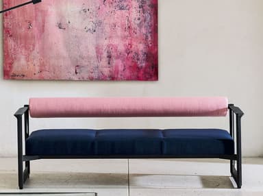 A modern bench featuring a minimalist black metal frame with dark blue upholstered seat cushions and a contrasting pink cylindrical bolster serving as the backrest. The frame includes integrated armrests. — 3D model