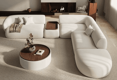 A multi-piece modular sectional sofa upholstered in a light, neutral fabric, featuring rounded edges and a low profile. One section includes a built-in wooden tray table. The arrangement is complemented by a separate, matching round coffee table with a wooden top. — 3D model