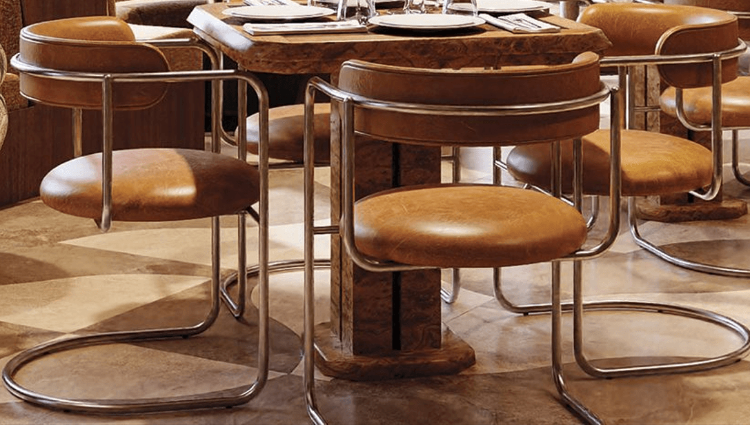 A modernist cantilever armchair featuring a tubular metal frame and upholstered seat and backrest. The frame is constructed from bent, polished metal tubing, forming integrated armrests and a distinctive cantilever base. The circular seat cushion and curved backrest are upholstered in a light brown or tan leather, providing a contrasting texture to the sleek metalwork. — 3D model