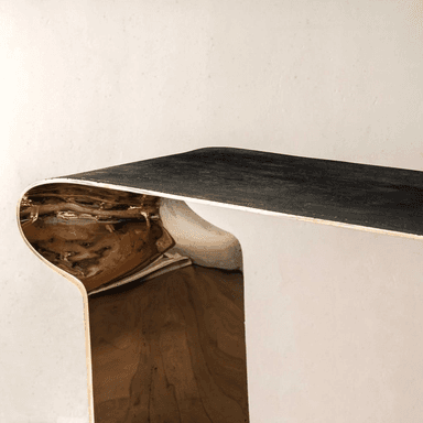 A modern sculptural console table featuring a distinctive two-tone finish. The table is formed from a single, continuous piece of material, creating a U-shaped or inverted C-shaped profile. The exterior surfaces exhibit a dark, patinated finish, while the interior curves are highly polished brass, creating a striking contrast. Its minimalist yet bold design makes it a prominent statement piece. — 3D model