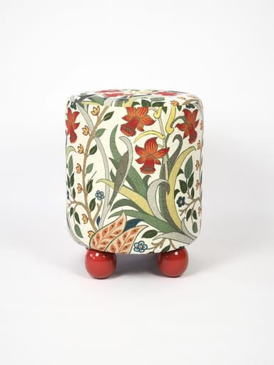 A compact, cylindrical ottoman upholstered in a multi-colored fabric featuring an intricate Arts and Crafts-inspired floral and botanical pattern. The main body of the ottoman rests on four short, spherical, brightly lacquered red feet, providing a contrasting base. The fabric design includes motifs of red flowers, green leaves, and delicate tendrils on an off-white background. — 3D model
