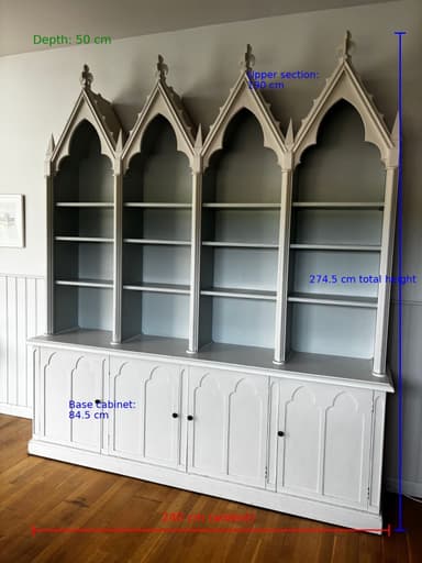 A tall, multi-sectioned bookcase hutch featuring a distinct Gothic Revival architectural style. The upper section consists of four open shelving bays, each topped with a prominent pointed arch and detailed tracery, culminating in decorative finials. The lower section provides enclosed storage with four paneled cabinet doors, each equipped with a small, dark spherical pull. The entire unit is rendered in a uniform light gray finish, suggesting painted wood or a similar material. The hutch sits on a base with a simple plinth. — 3D model