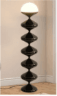 A tall, modern floor lamp featuring a sculptural base composed of six stacked, bulbous, glossy black segments, tapering towards the top. It is crowned with a luminous, hemispherical light diffuser, emitting a warm glow. — 3D model