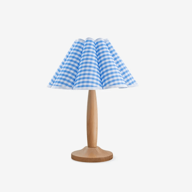 A table lamp featuring a light-toned wooden base and a distinctive pleated fabric shade. The base consists of a circular platform and a tapered, smooth stem. The conical shade is made from blue and white gingham-patterned fabric, arranged in neat, vertical pleats that create a scalloped edge along the bottom. The overall design is clean and modern with a touch of playful charm. — 3D model