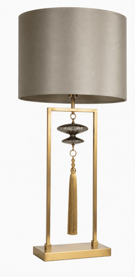 A contemporary table lamp with a rectangular base and a vertical rectangular frame. A drum-shaped lampshade in a neutral taupe color sits atop the frame. Suspended within the frame is a decorative element consisting of two stacked, ribbed glass orbs in a smoked grey color, a beaded section, and a golden tassel. — 3D model