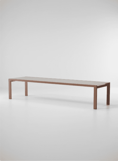 A long, minimalist rectangular coffee table featuring a slim profile. The table consists of a reddish-brown matte metal frame that forms the legs and supports, topped with a lighter, contrasting surface, possibly glass or a composite material. Its design emphasizes clean lines and a contemporary aesthetic. — 3D model