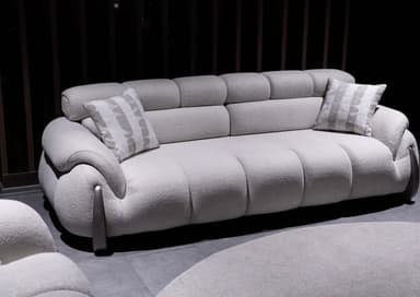 A modern, large, light gray upholstered sofa featuring distinct rounded, segmented cushions and a channel-tufted backrest. The base has visible wooden or dark-colored curved supports. Two decorative throw pillows are included. — 3D model