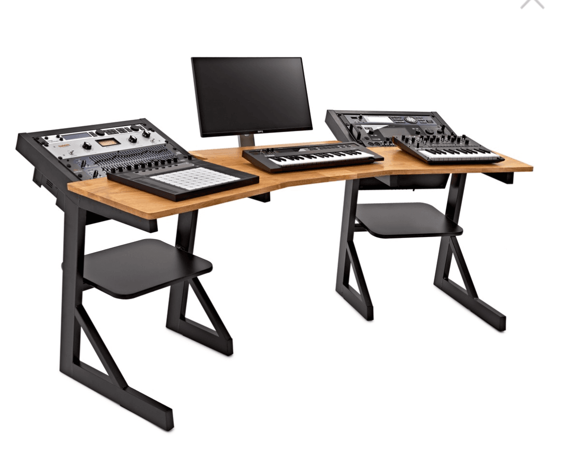 A long, ergonomic studio desk designed for audio production. The desk features a natural wood-finished desktop with a gently curved front edge. It has a modular design with angled black metal legs and integrated shelves beneath the main surface. The desk is equipped with several pieces of audio equipment, including a monitor, a mixing console, and multiple keyboard controllers. — 3D model