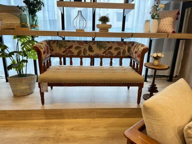 A traditional-style upholstered settee or bench featuring a dark wooden frame, a tufted cream-colored seat cushion, and armrests and backrest upholstered in a floral fabric pattern with green, red, and cream hues. The frame has turned legs and spindle details along the backrest and decorative nailhead trim. — 3D model