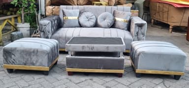 A contemporary grey velvet sofa featuring distinct channel tufting on the seat back and along the front base, complemented by button tufting on the exterior arms. The sofa is accented with a polished gold-finished trim that runs along the bottom edge, just above its dark wooden feet, which are also capped with gold accents. It includes four decorative throw pillows: two square pillows with a prominent gold fabric band, and two round, button-tufted pillows. — 3D model