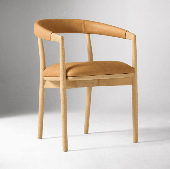 A contemporary armchair with a wooden frame and a tan leather seat and backrest. The chair features a gently curved back and arms, supported by four tapered wooden legs. The frame appears to be made of light-colored wood, possibly beech or ash, with a smooth, natural finish. The upholstery is a smooth, possibly genuine leather, in a warm tan color. — 3D model