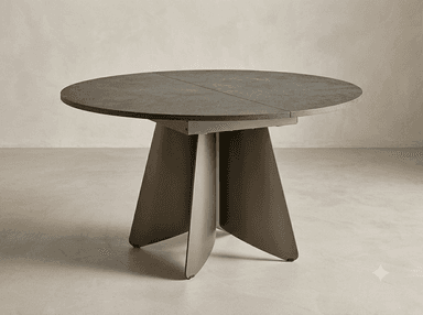 A modern round dining table featuring a dark, textured tabletop, which appears to be made from a sintered stone or ceramic material, supported by a distinctive, sculptural pedestal base crafted from dark bronzed metal. The tabletop shows a visible seam, suggesting it may be extendable. The base consists of four robust, trapezoidal legs that converge towards the center, providing stability and a contemporary aesthetic. — 3D model