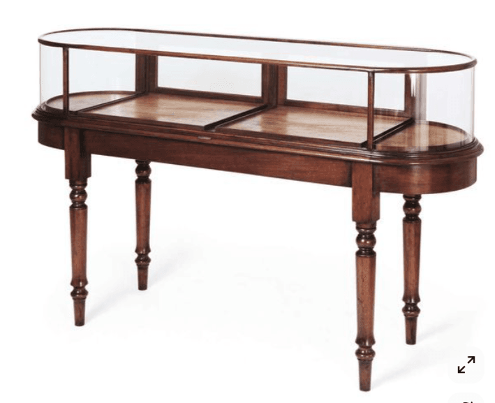 An antique-style display cabinet featuring an elongated oval glass top with a frosted finish, supported by a dark wood frame. The cabinet has four turned legs and a lower shelf, also in dark wood, providing additional storage or display space. The overall design suggests a piece of furniture intended for showcasing decorative items. — 3D model