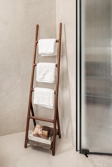A dark brown wooden leaning ladder-style towel rack featuring three rounded rungs for hanging textiles and an integrated rectangular base shelf for additional storage. The design is characterized by smooth, curved lines and a minimalist aesthetic. — 3D model