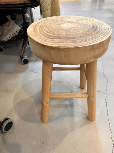 A light-colored solid wood stool with a thick, round seat exhibiting prominent growth rings, supported by three splayed, tapered legs with crossbar bracing. — 3D model