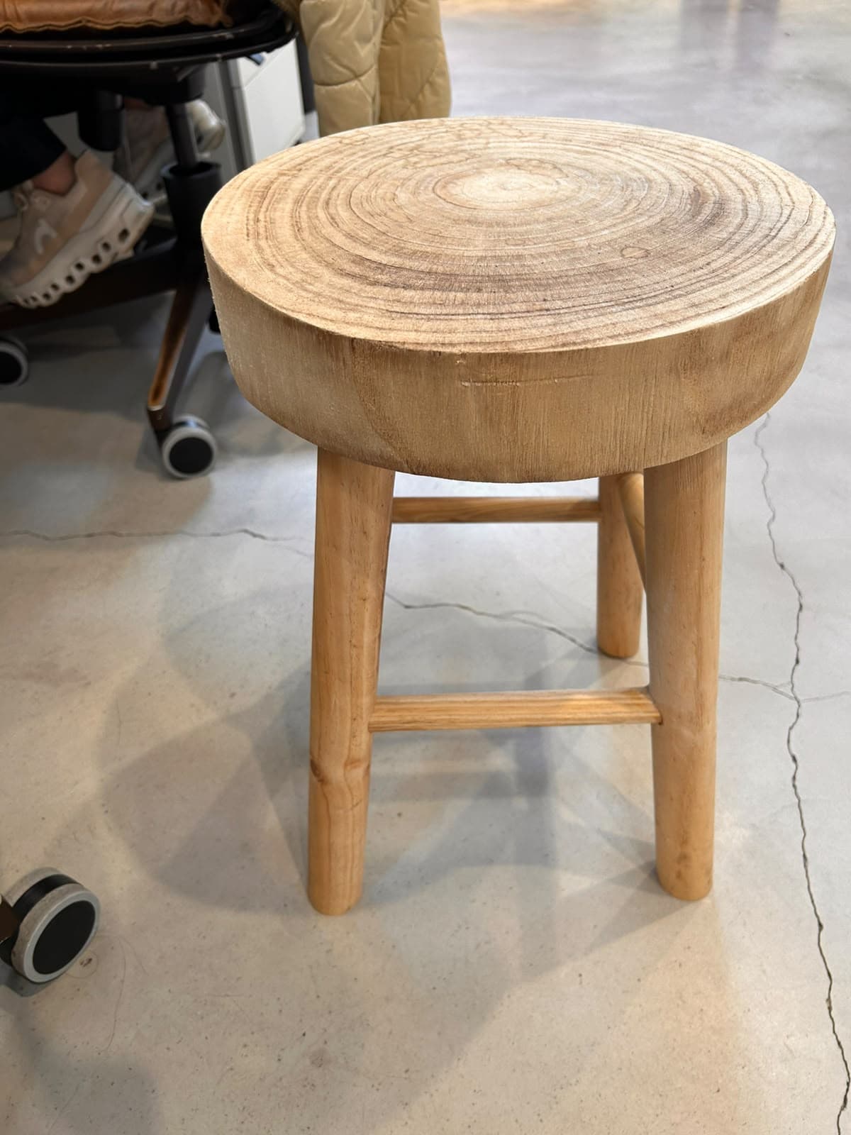 A light-colored solid wood stool with a thick, round seat exhibiting prominent growth rings, supported by three splayed, tapered legs with crossbar bracing. — 3D model