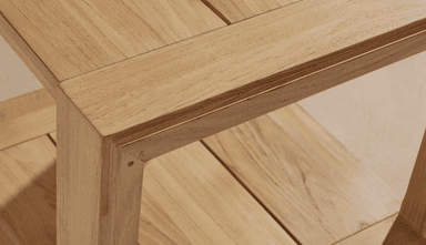 A detailed close-up shot of the corner of a two-tiered console table constructed from light-toned natural wood. The top surface features a framed design with parallel wooden planks. Directly below, a second shelf is visible, also made of parallel wooden planks, creating a functional two-tiered structure. The table leg is stout and rectangular, connected to the top and lower shelf with visible joinery, suggesting a sturdy construction. The wood exhibits a fine, consistent grain with a light, natural finish. — 3D model