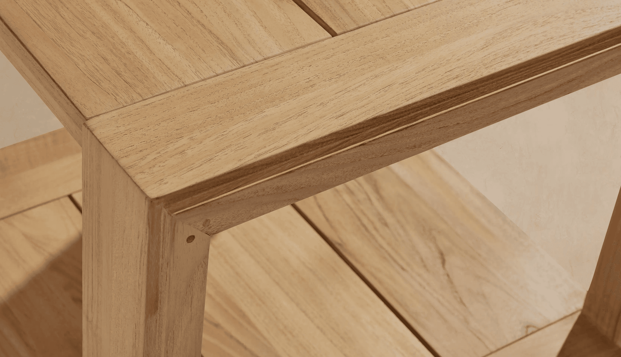 A detailed close-up shot of the corner of a two-tiered console table constructed from light-toned natural wood. The top surface features a framed design with parallel wooden planks. Directly below, a second shelf is visible, also made of parallel wooden planks, creating a functional two-tiered structure. The table leg is stout and rectangular, connected to the top and lower shelf with visible joinery, suggesting a sturdy construction. The wood exhibits a fine, consistent grain with a light, natural finish. — 3D model