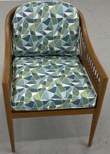 A barrel-back armchair featuring a warm-toned wooden frame, likely teak or oak, with distinctive woven or rope detailing along the arms and backrest. The chair is upholstered with removable seat and back cushions in a textured, multi-tonal green, white, and blue striped fabric. Its design combines elegant curves with a relaxed, tropical-modern aesthetic. — 3D model