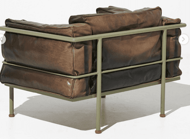 A contemporary armchair featuring a tubular metal frame and plush, overstuffed leather cushions. The frame has a matte green finish and supports the seat, back, and armrest cushions. The leather appears to be distressed or aged, with variations in color and texture. The armchair has a low profile and appears designed for comfort. — 3D model