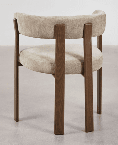 A contemporary accent chair with a curved backrest and seat, upholstered in a textured, light-colored fabric. The chair features a distinctive frame constructed from dark wood, with four legs providing support. The arms are integrated into the backrest structure. — 3D model